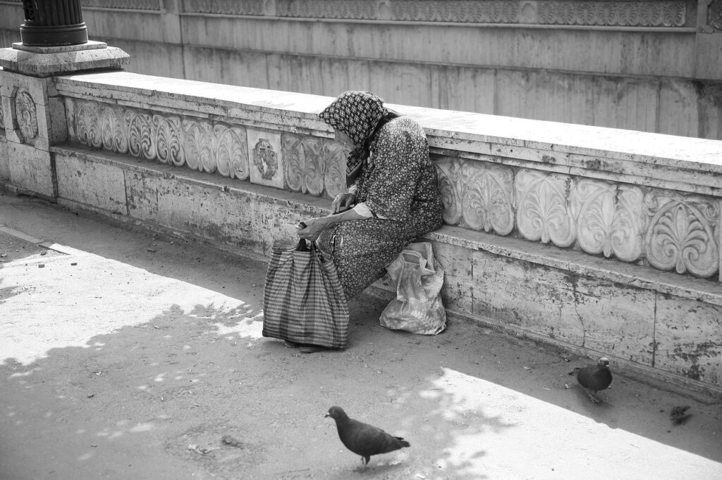 Mujer mayor pobre sentada en una plaza, imagen de la miseria